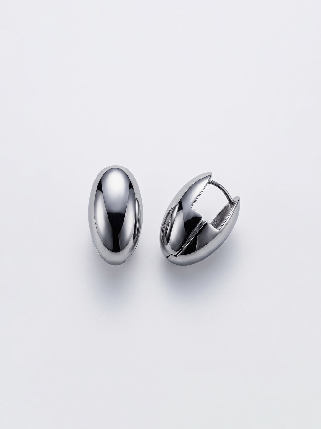 A pair of polished silver-toned metal egg shaped huggie hoop earrings on a clean, light gray background.