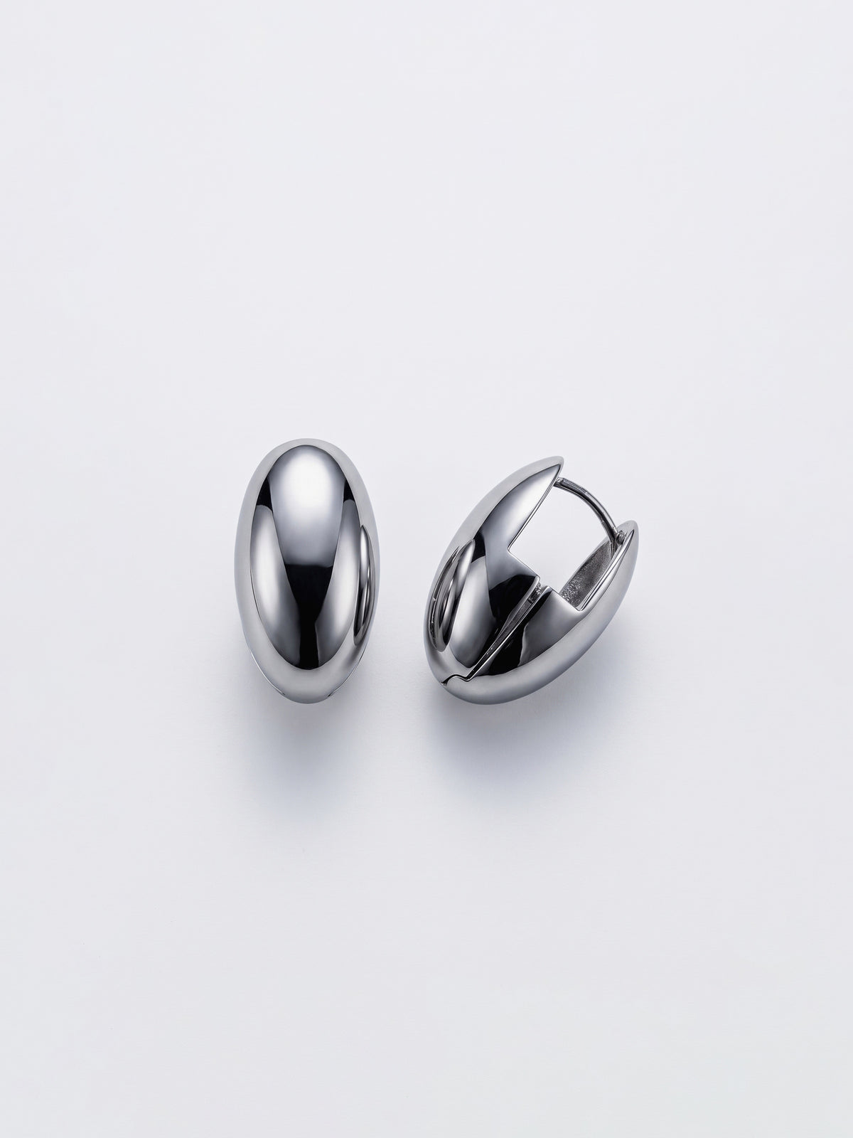 A pair of polished silver-toned metal egg shaped huggie hoop earrings on a clean, light gray background.