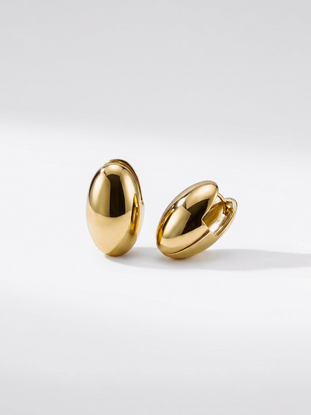 A pair of gold egg shaped earrings with a polished, metallic finish, with hindge closure displayed against a clean white background