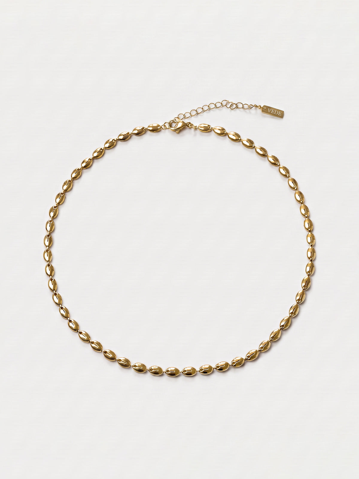 A gold-toned chain necklace with a textured, elongated oval link design, displayed on a clean white background. The necklace features an adjustable lobster clasp and a fine extension chain with a small brand tag.