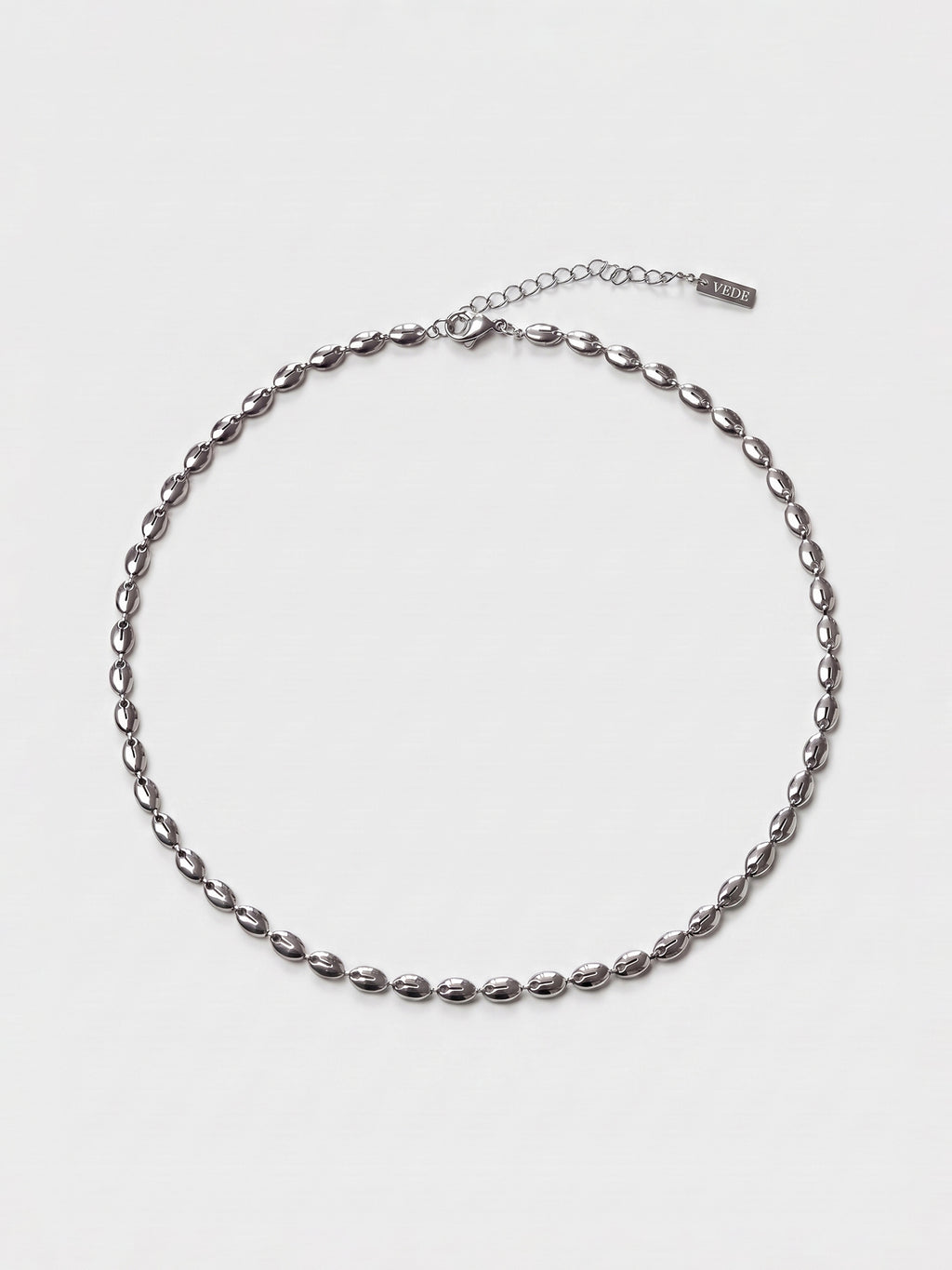 A silver-toned chain necklace with a textured, elongated oval link design, displayed on a clean white background. The necklace features an adjustable lobster clasp and a small brand tag near the clasp.