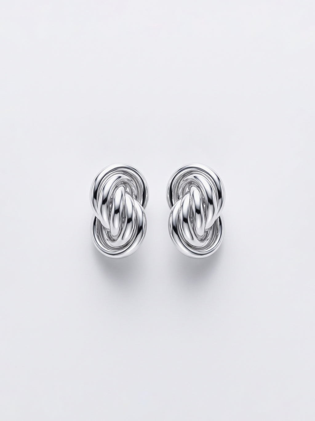 A pair of silver-toned knot stud earrings with a polished metallic finish, displayed on a clean, light gray background.