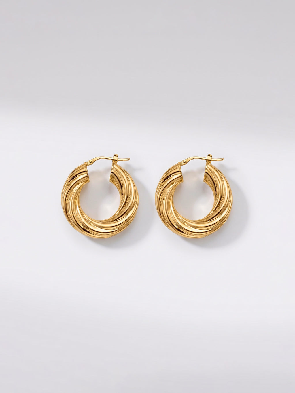 A pair of gold-toned twisted hoop earrings with a polished finish, displayed on a clean light gray background.